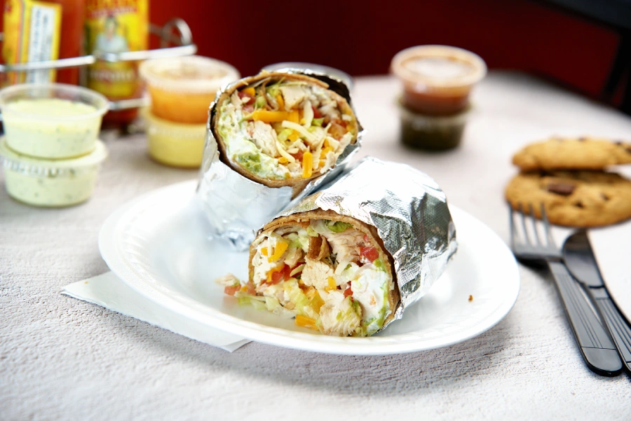 Healthy Food restaurant in Kendall, Delicious chicken burrito cut in half and served on a white plate with sauces and cookies